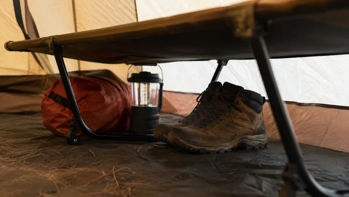 Boots, a lantern, and a small dry bag stored in the open space underneath a camping cot