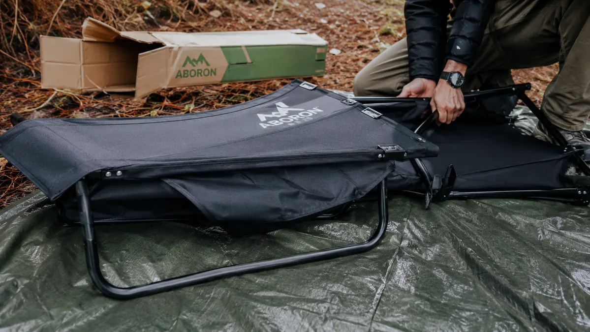 Camping cot folded and leaning against a tent stake bag with a small bent leg tube visible