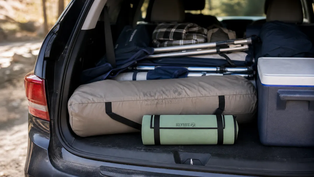 Packed cot bag next to a rolled sleeping pad in the back of a car trunk