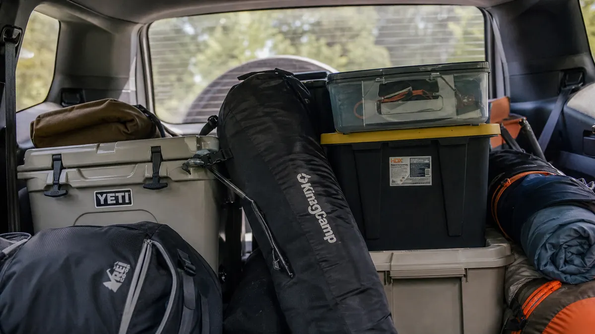 The ALPHA CAMP chair folded and strapped into a tightly packed SUV cargo area alongside coolers and bins