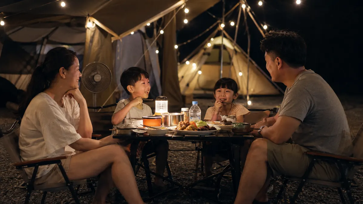 Family sitting around a small camp table at night with string lights powered by a portable power station