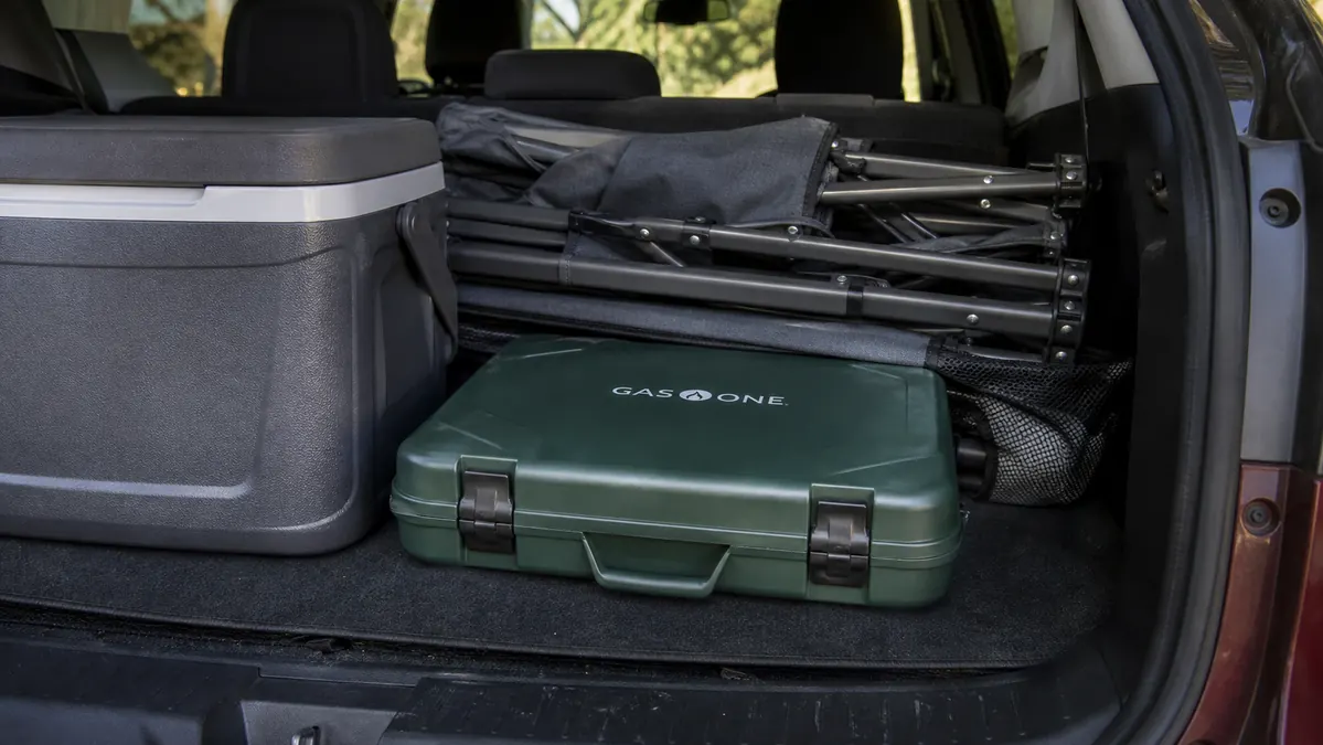 The Gas One stove folded flat and latched shut, packed next to a cooler and camp chairs in the back of an SUV