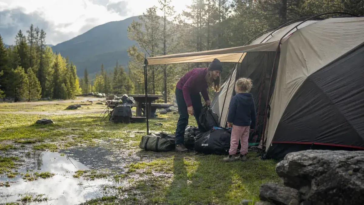 Family unloading dry gear from a tent vestibule the morning after an overnight rainstorm