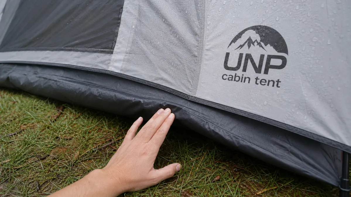 Close-up of a hand pressing down on the tub-style tent floor seam to show it stays raised above puddled ground